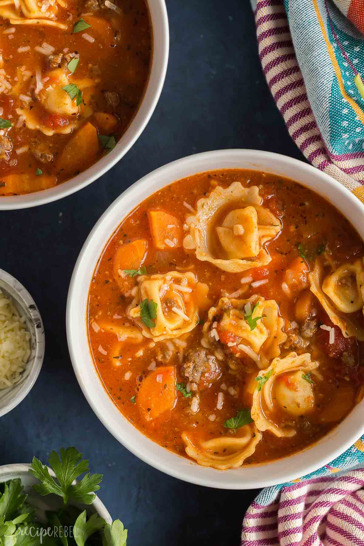 overhead image of a bowl of sausage tortellini soup on blue background.