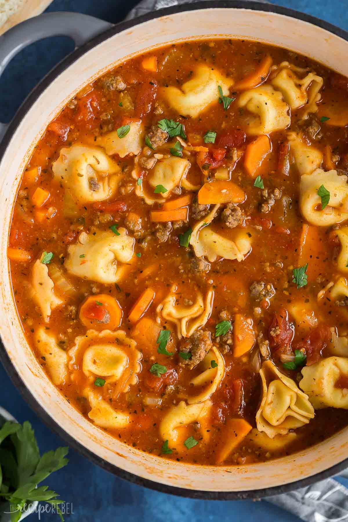 close up overhead image of tortellini soup with sausage in tomato broth.

