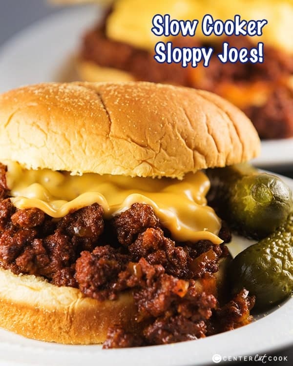 ground beef crock pot sloppy joes close up on white bun with melted cheese and pickles on the side