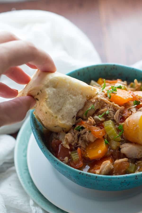 instant pot tuscan chicken stew in bright blue bowl with crusty bread being dipped in it