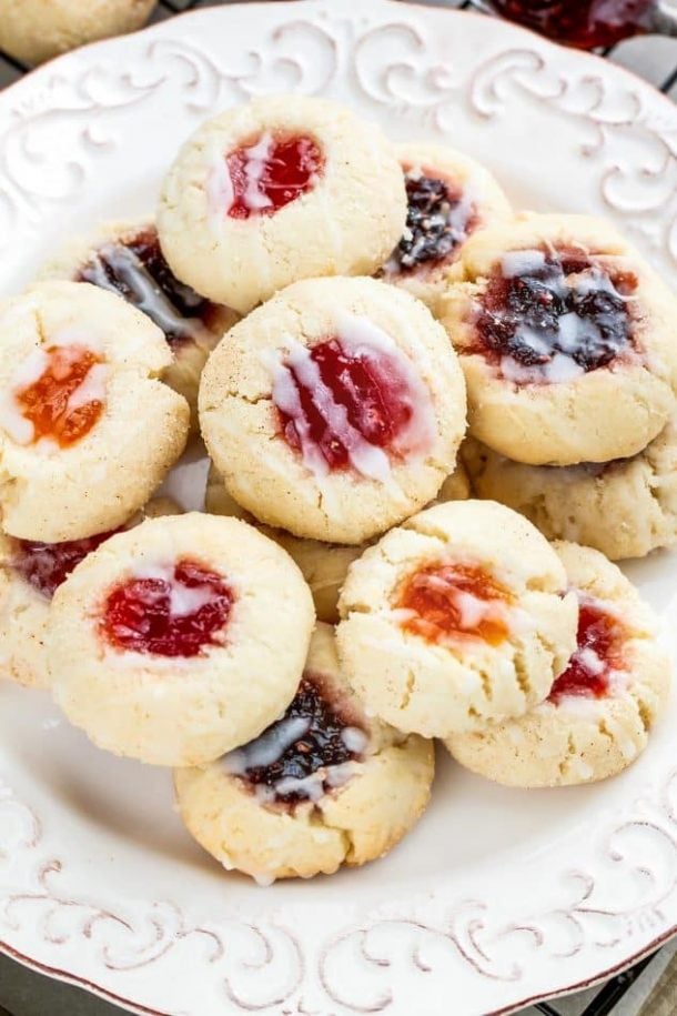 shortbread thumbprint christmas cookies with different types of jam filling and white glaze