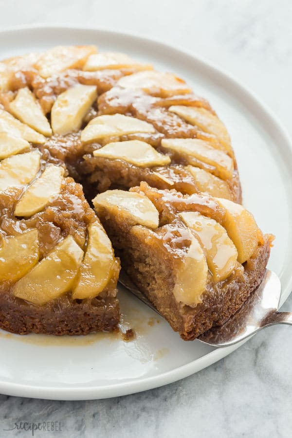 slice of apple upside down cake being pulled out of whole cake on metal server