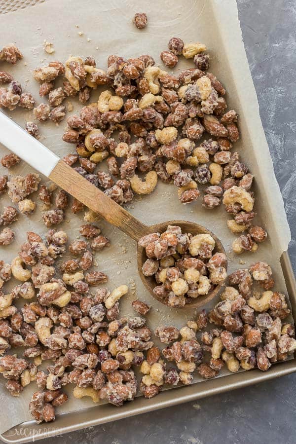 These Easy Candied Nuts are just 6 ingredients and less than 30 minutes start to finish! They are sweet and salty with a hint of cinnamon -- perfect for an edible holiday gift! #nuts #pecans #almonds #gift #Christmas #baking candied nuts on sheet pan lined with parchment paper overhead with wooden spoon on pan