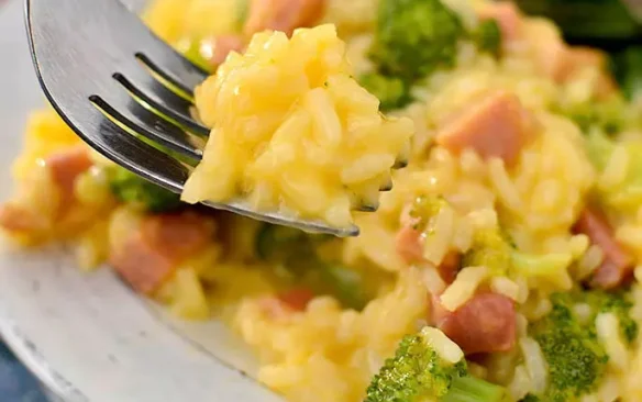 A forkful of cheesy rice with ham and broccoli.