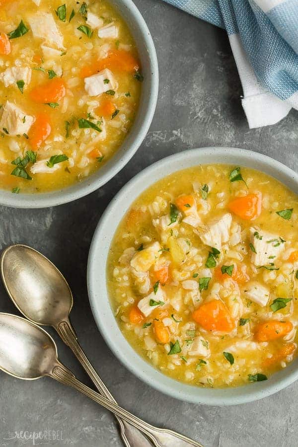 chicken rice soup in bowls overhead on grey background with two spoons on the side