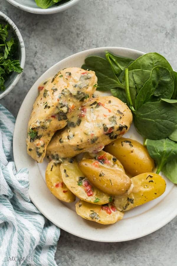 italian crockpot chicken and potatoes on plate with fresh spinach on the side on a grey background