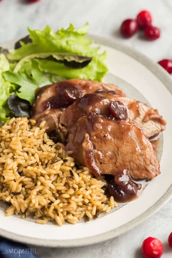 crock pot pork tenderloin on a grey plate with seasoned rice and salad and fresh cranberries in the background