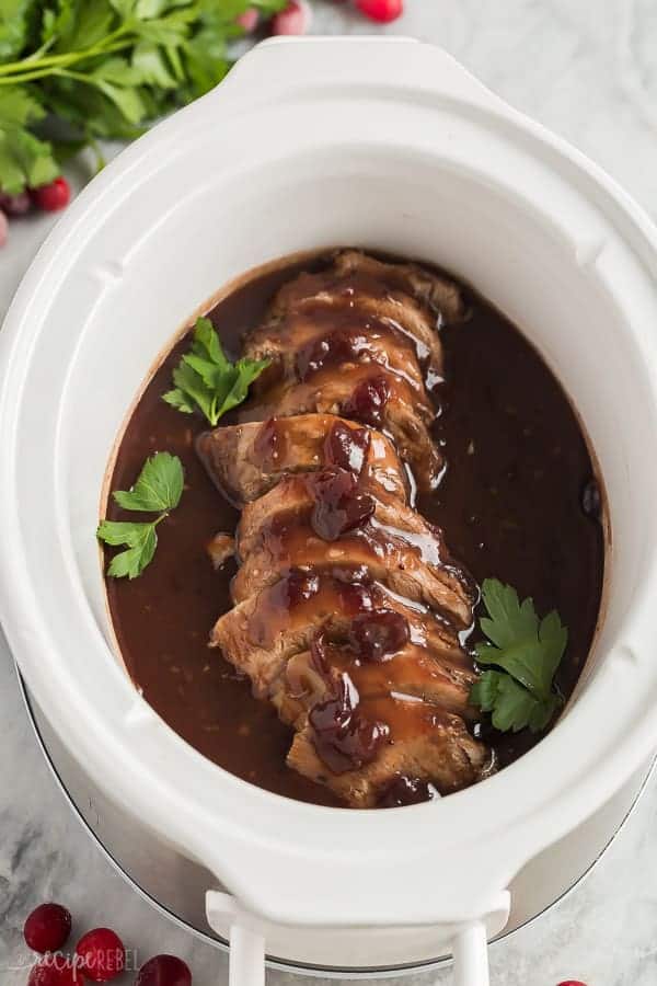 crock pot pork tenderloin with cranberry sauce in slow cooker and fresh parsley garnish
