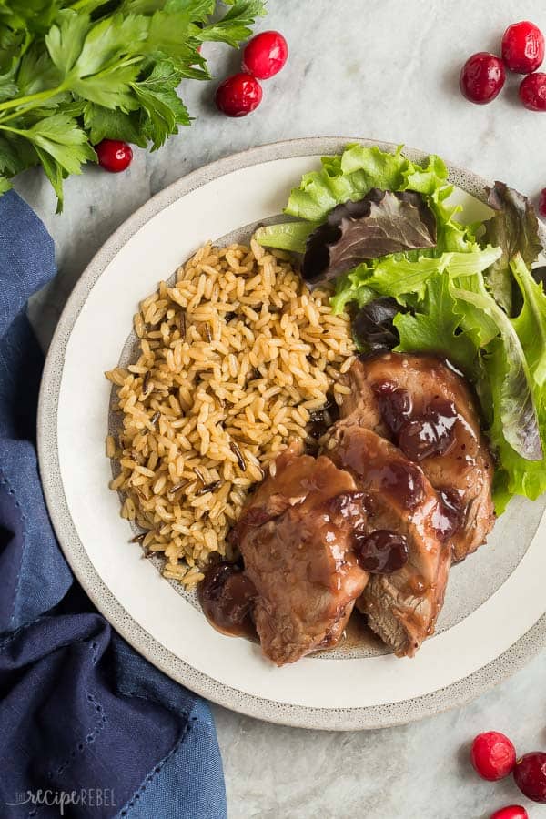 crock pot pork tenderloin with cranberries plated on grey plate with rice and fresh greens
