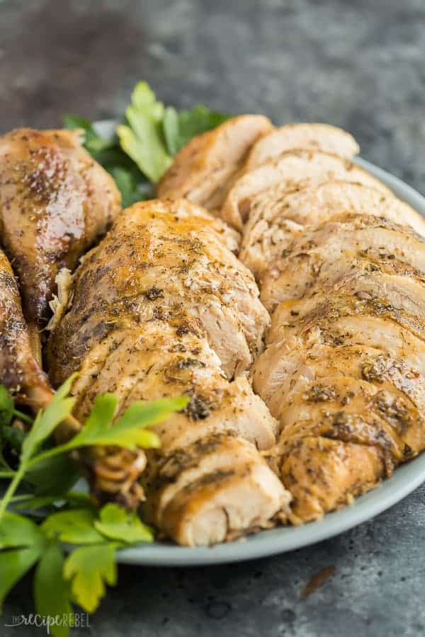 crockpot turkey sliced on large plate on dark grey background with parsley sprigs as garnish