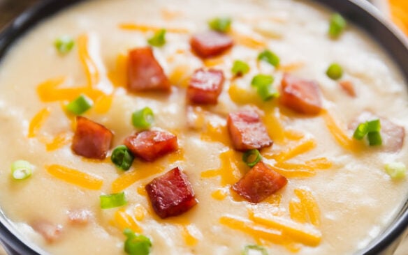 A bowl of creamy ham and potato soup topped with bits of ham and chives.