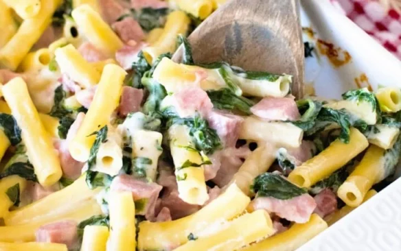 Cheesy ham and spinach casserole with a wooden spoon.