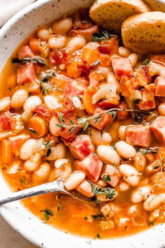 A bowl of ham and bean soup garnished with thyme.