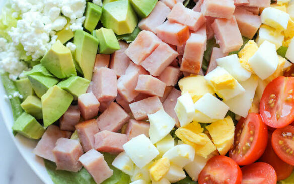 Rows of ingredients make up a ham cobb salad in a bowl.