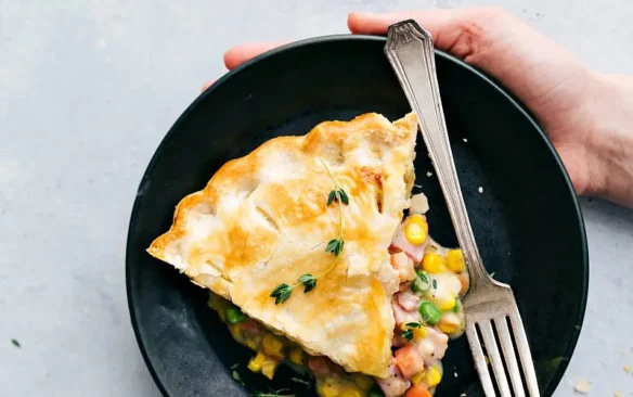 Top view of a slice of ham pot pie on a plate held by two hands.