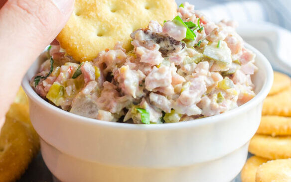 A cracker is dipped into a bowl of ham salad.