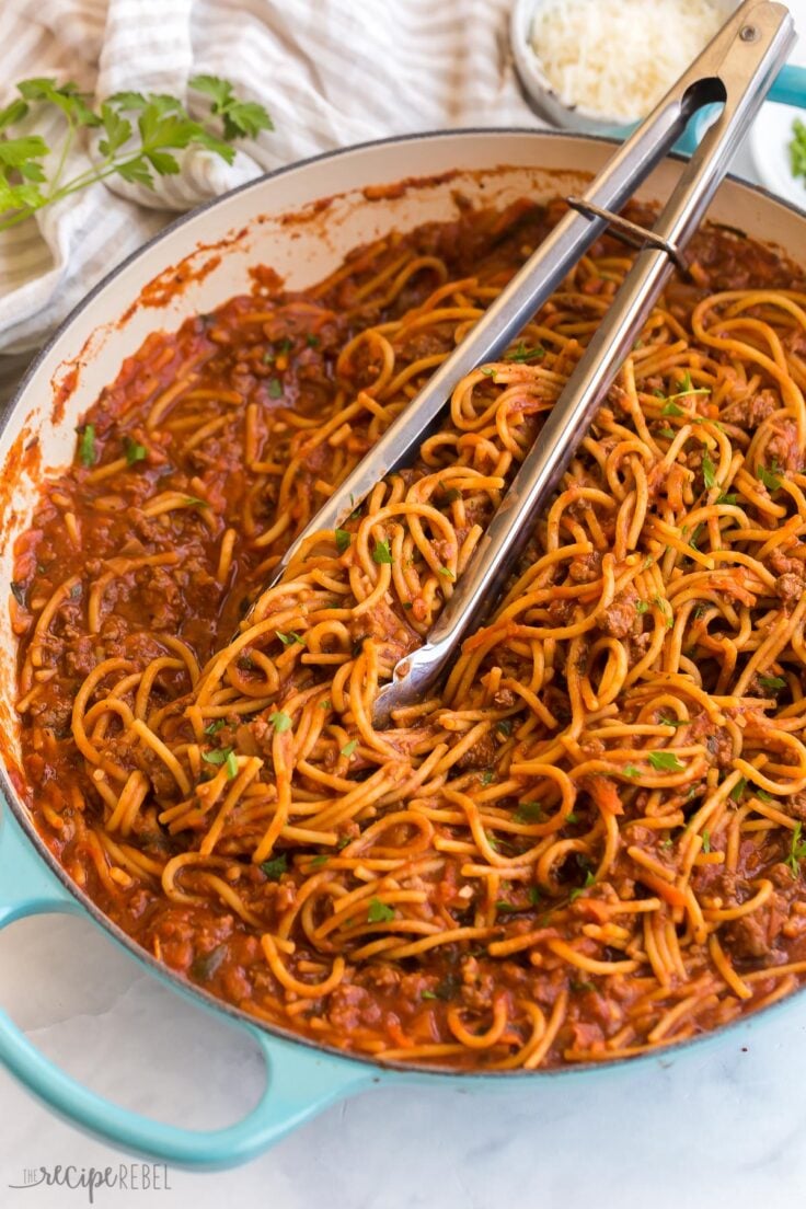 close up image of one pot spaghetti and meat sauce with tongs stuck in