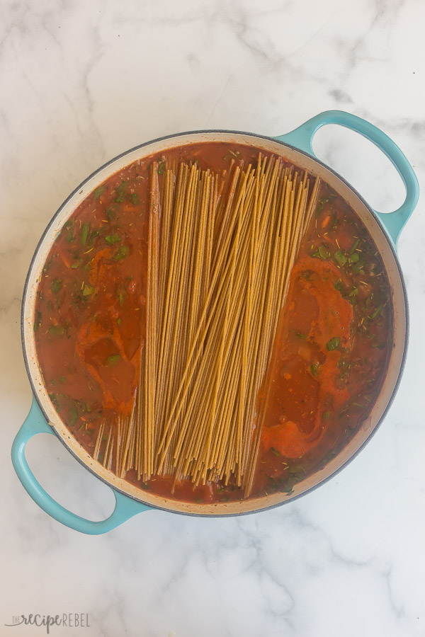 dry spaghetti added to spaghetti sauce in pan