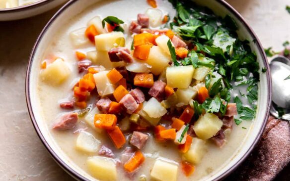 A bowl of ham bone soup topped with ham and veggies, surrounded by bowls of seasonings.