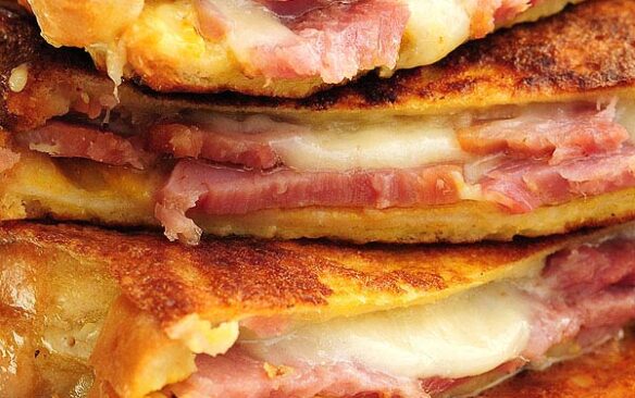A stack of grilled Monte Cristo sandwiches with ham and melted cheese.