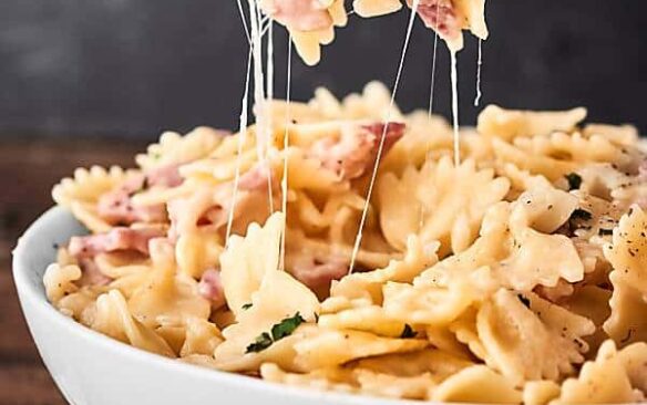A forkful of ham and cheese pasta is lifted from a bowl.