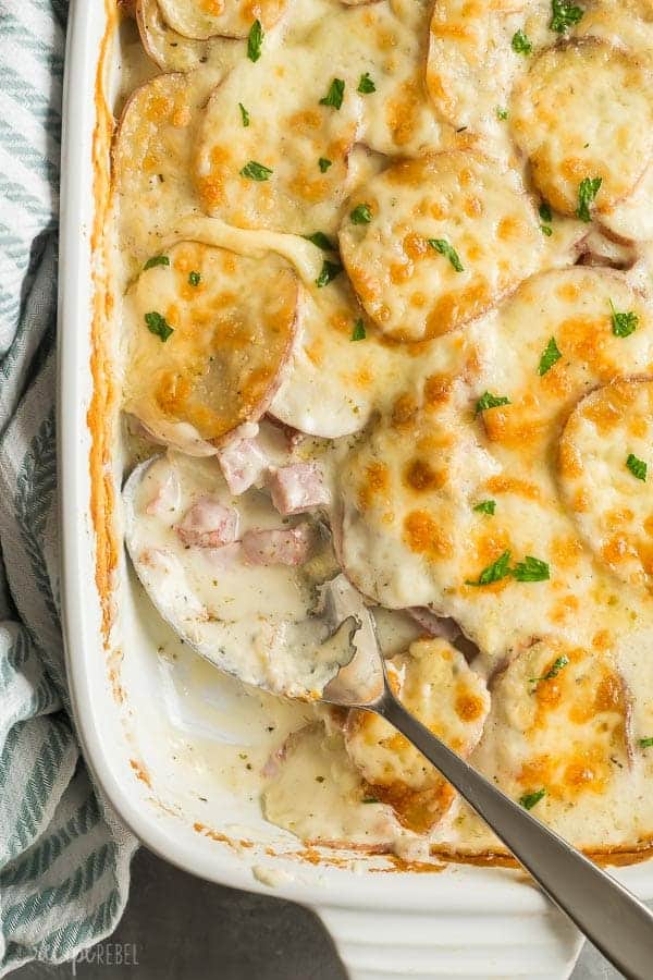 cheesy scalloped potatoes and ham close up with metal spoon stuck in the corner