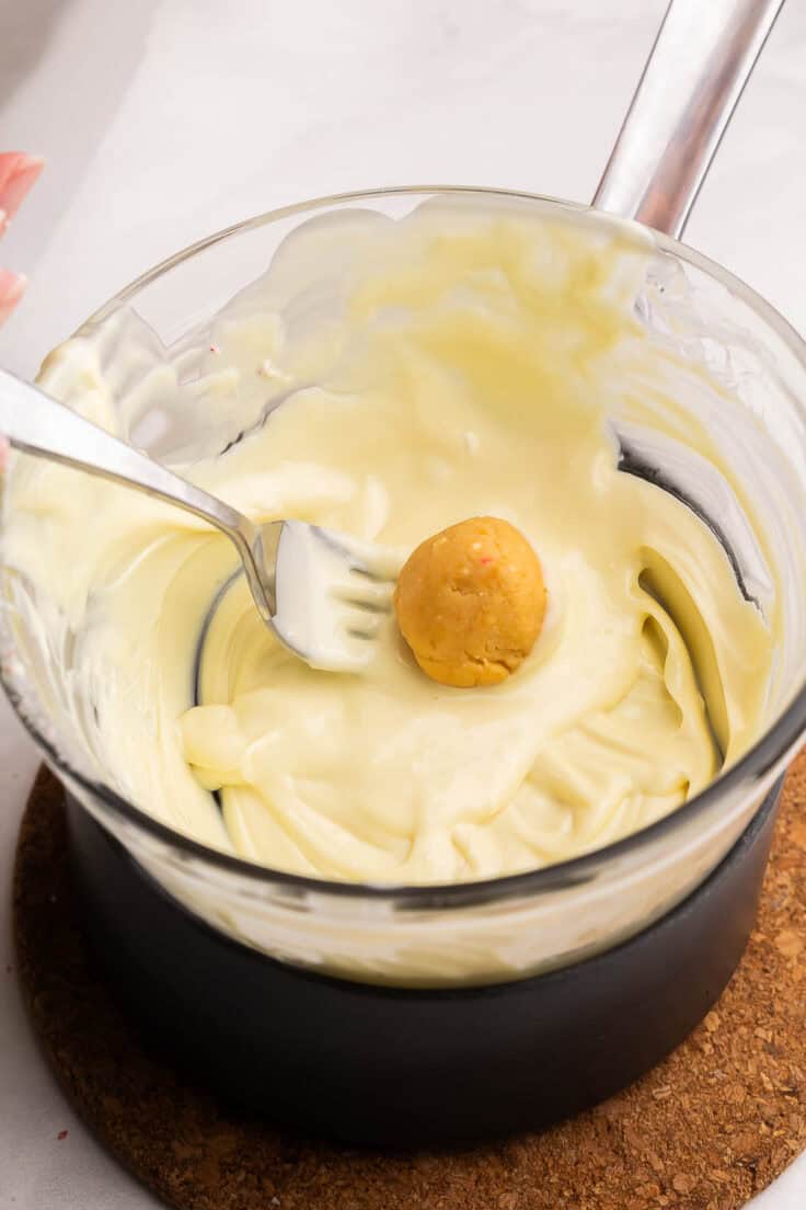 golden oreo truffles being dipped in white chocolate.