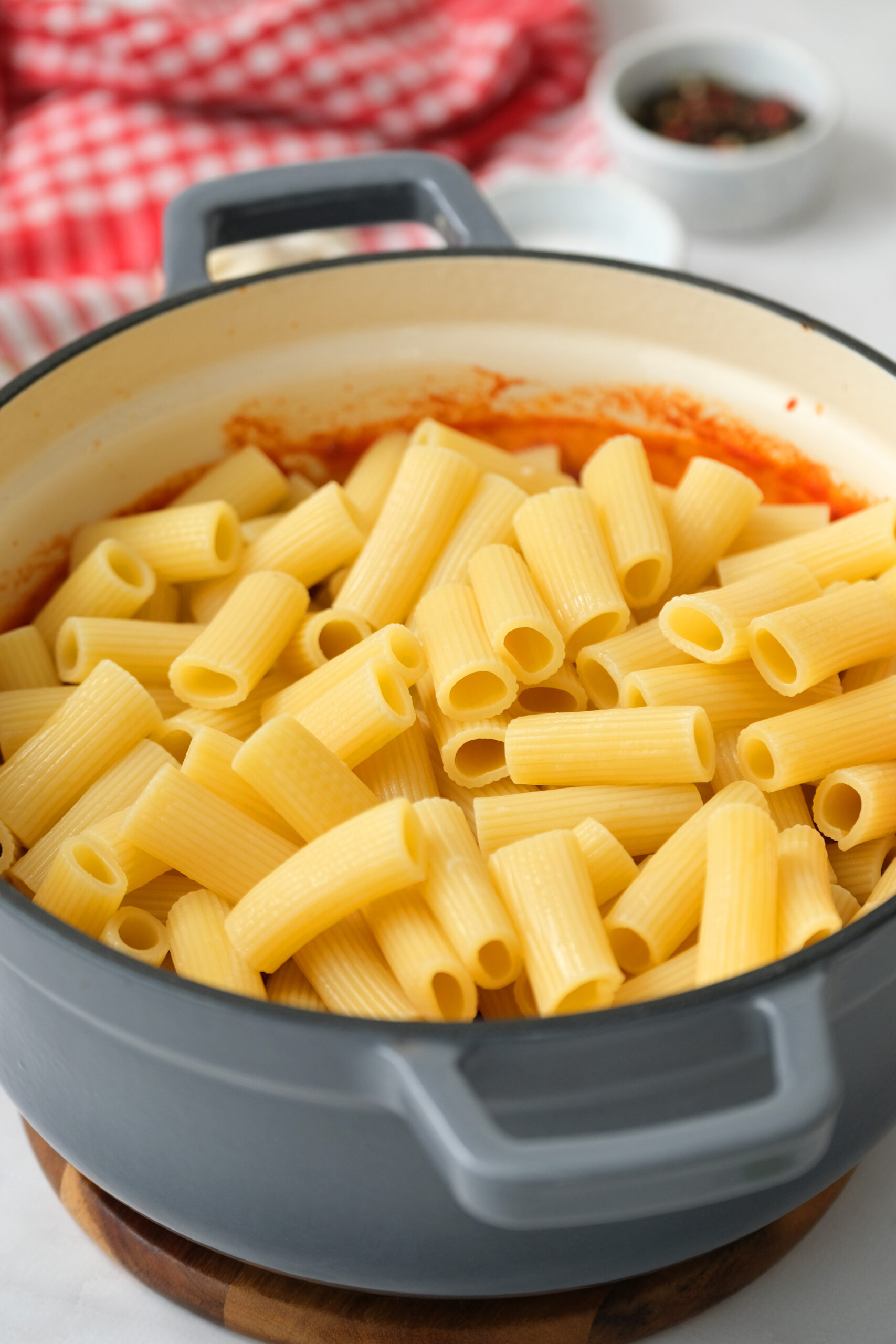 cooked rigatoni being added to sauce in pot.
