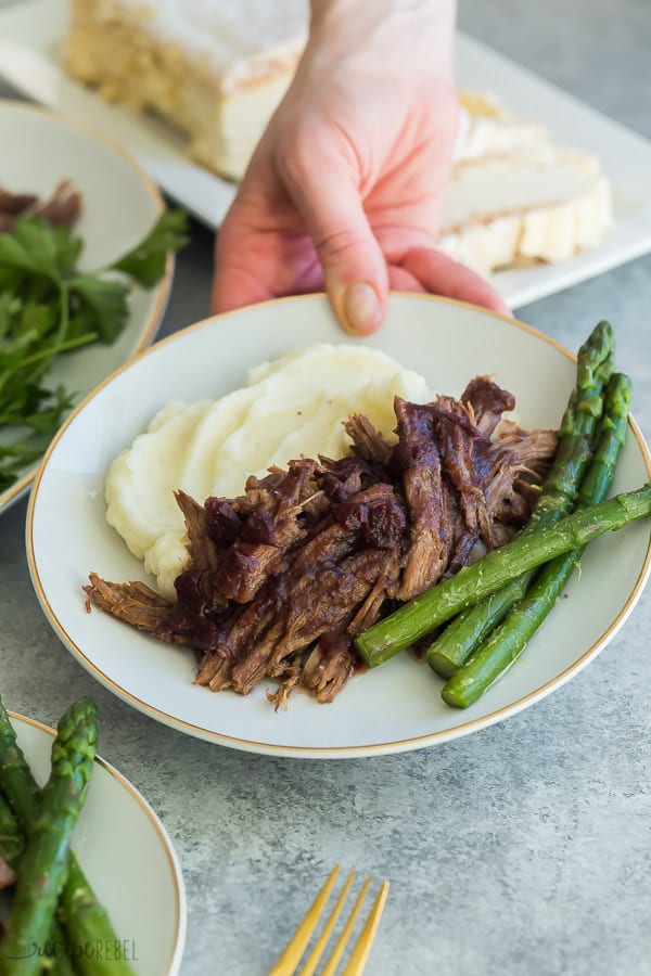 instant pot roast beef with asparagus and mashed potatoes on white plate held in a hand