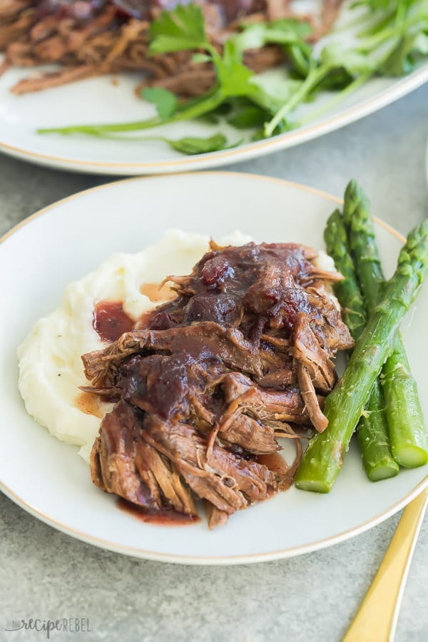 instant pot roast beef with cranberry gravy on a white plate with mashed potatoes and asparagus