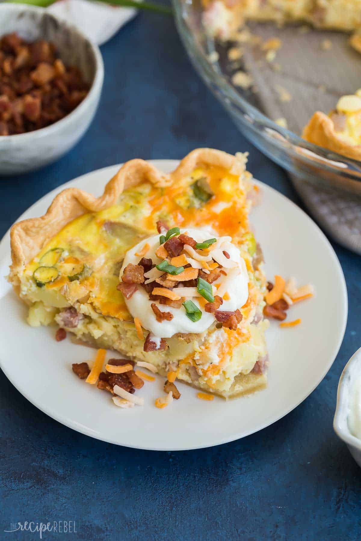 This Loaded Baked Potato Quiche is easy and full of flavor! It's the perfect easy quiche recipe for the holidays or a weeknight dinner. #breakfast #quiche #recipe | easter brunch | holiday brunch | breakfast recipes | quiche recipes | baked potatoes | easy dinner ideas one piece of baked potato quiche on a white plate with sour cream and bacon on top.