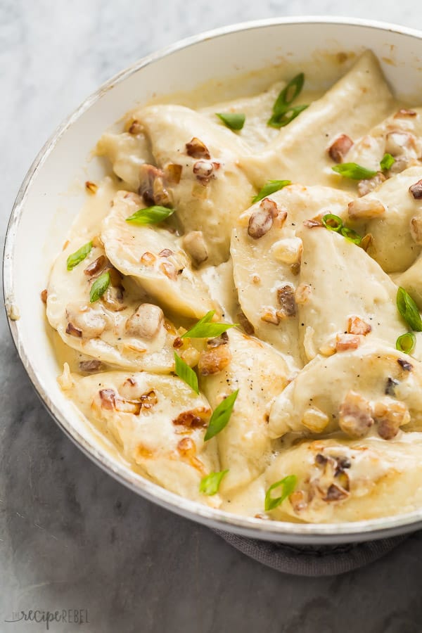 perogies in white pan with bacon and green onions in creamy sauce