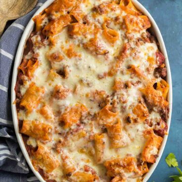 rigatoni pasta bake in white baking dish with blue towel on the side.