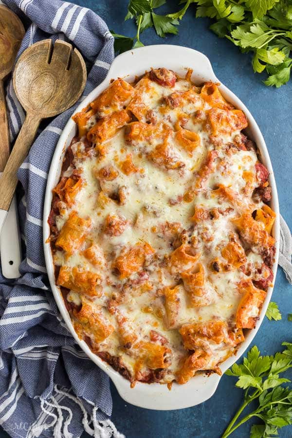 rigatoni pasta bake overhead in white baking dish on dark blue background with fresh parsley on the side