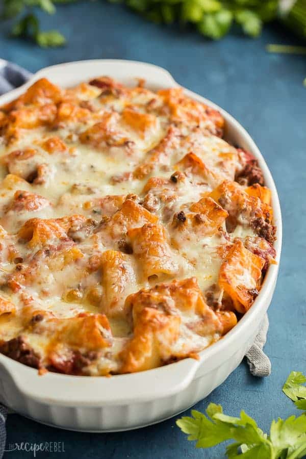 rigatoni pasta bake ground beef casserole in white oval baking dish on dark blue background