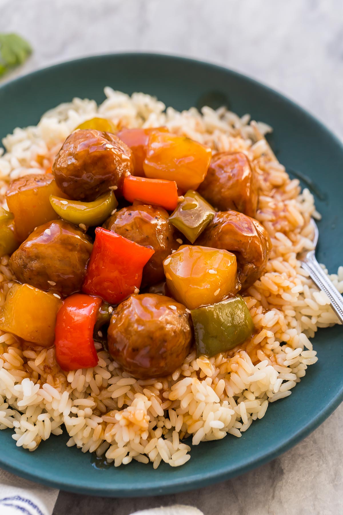close up image of sweet and sour crockpot meatballs on a plate of rice