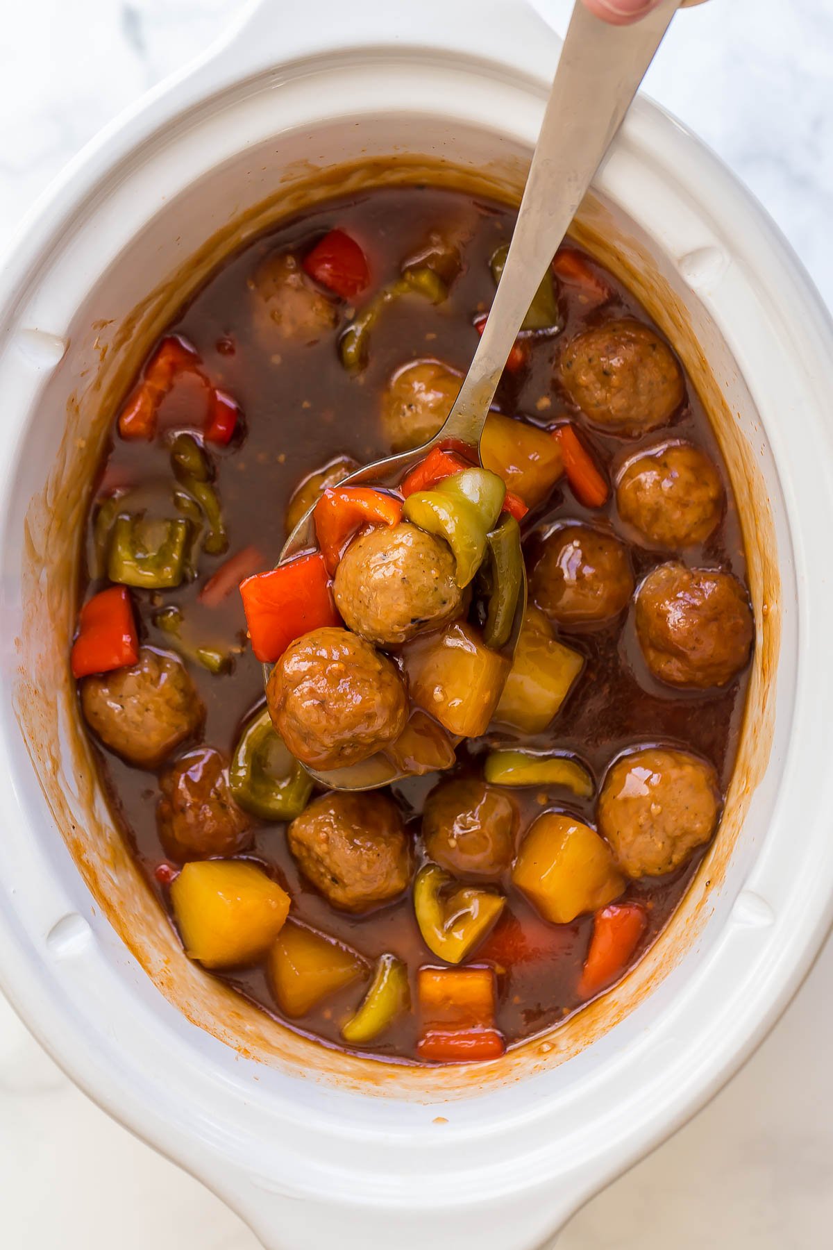 These Sweet and Sour Crockpot Meatballs are made with fresh or frozen meatballs and covered in the best pineapple sweet and sour sauce! An easy slow cooker meal! #slowcooker #crockpot #meatballs overhead image of crockpot meatballs with pineapples and peppers