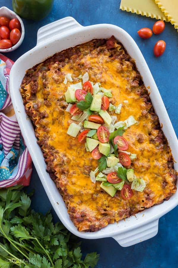 taco lasagna recipe overhead in white baking dish with avocado chunks and fresh tomatoes on top