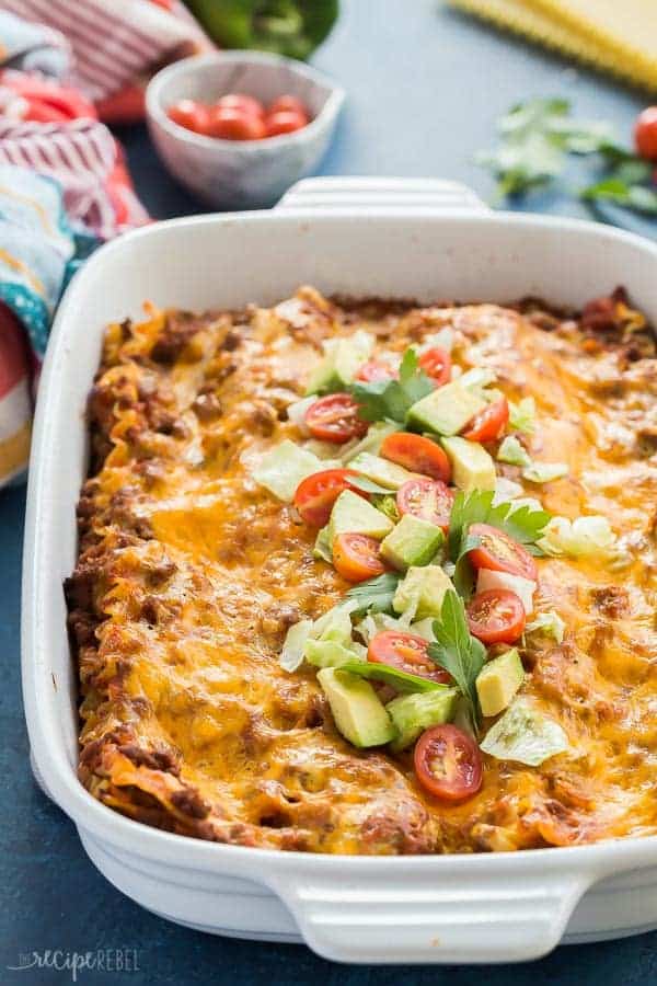 taco lasagna recipe in white pan with avocado fresh tomato and cilantro on top