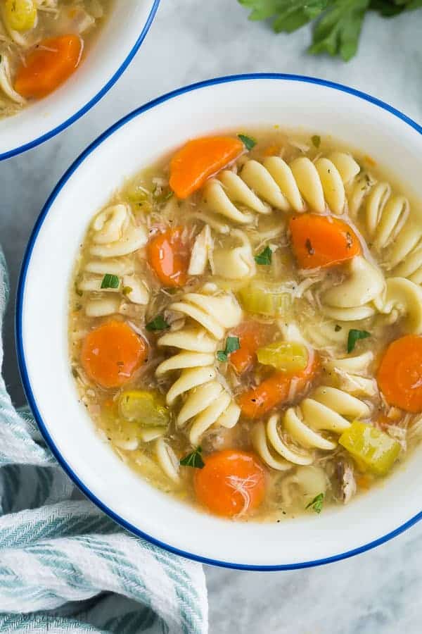 turkey noodle soup close up in white bowl with blue rim overhead