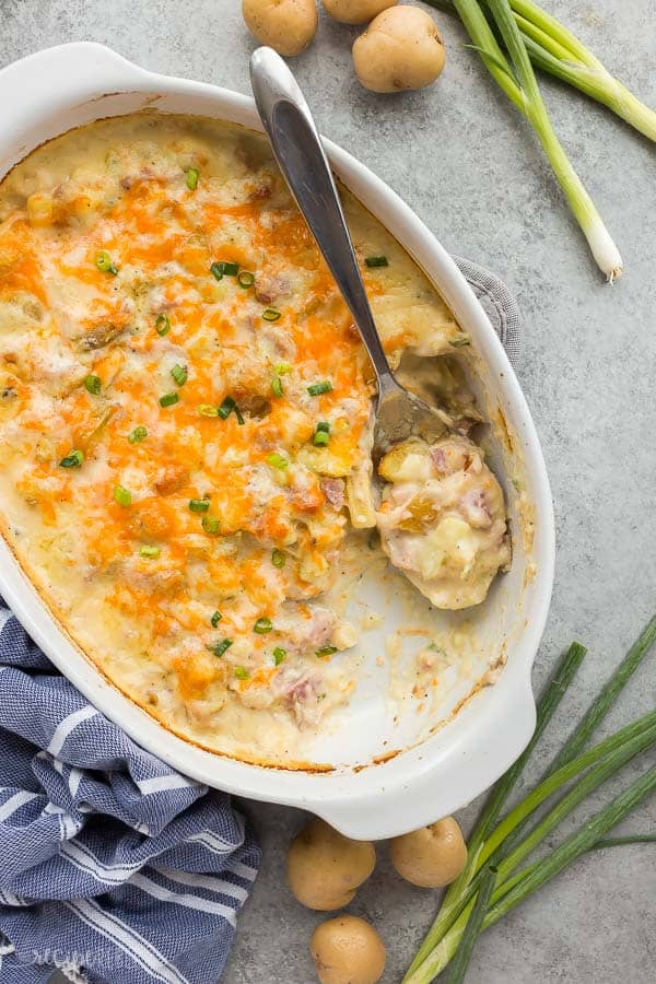 twice baked potato casserole overhead with metal spoon scooping some and green onions and potatoes on the side