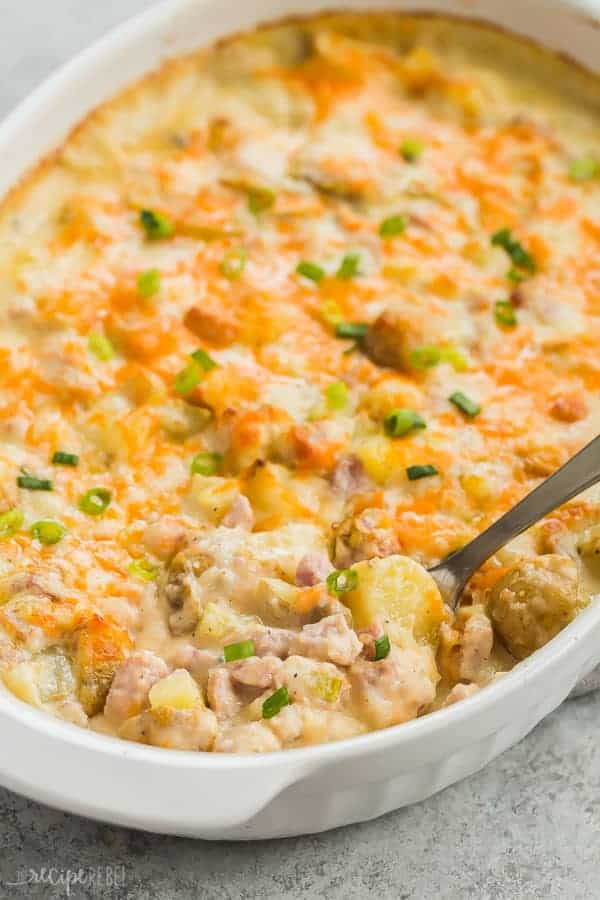 twice baked potato casserole in white pan with metal spoon scooping some in the corner