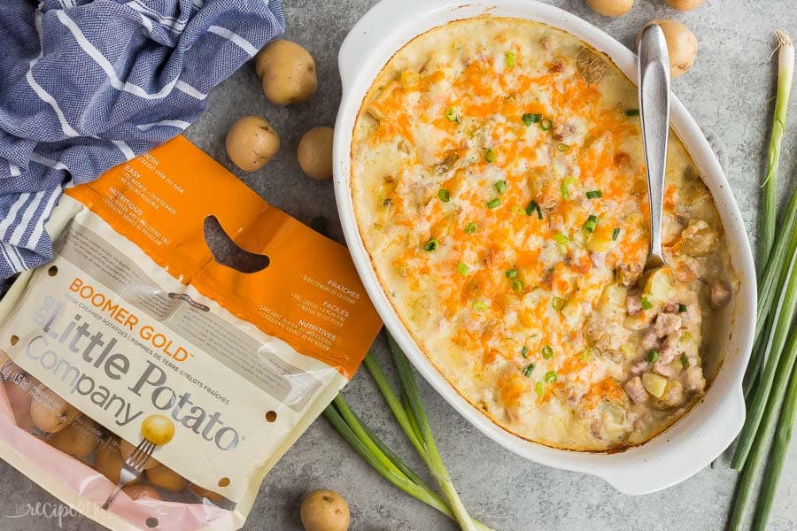 twice baked potato casserole with ham in white baking dish with bag of little potatoes and green onions on the side