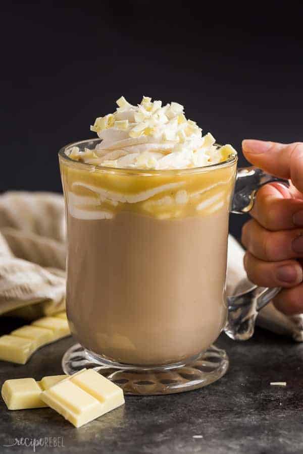 white chocolate mocha in glass mug with whipped cream and white chocolate shavings on black background