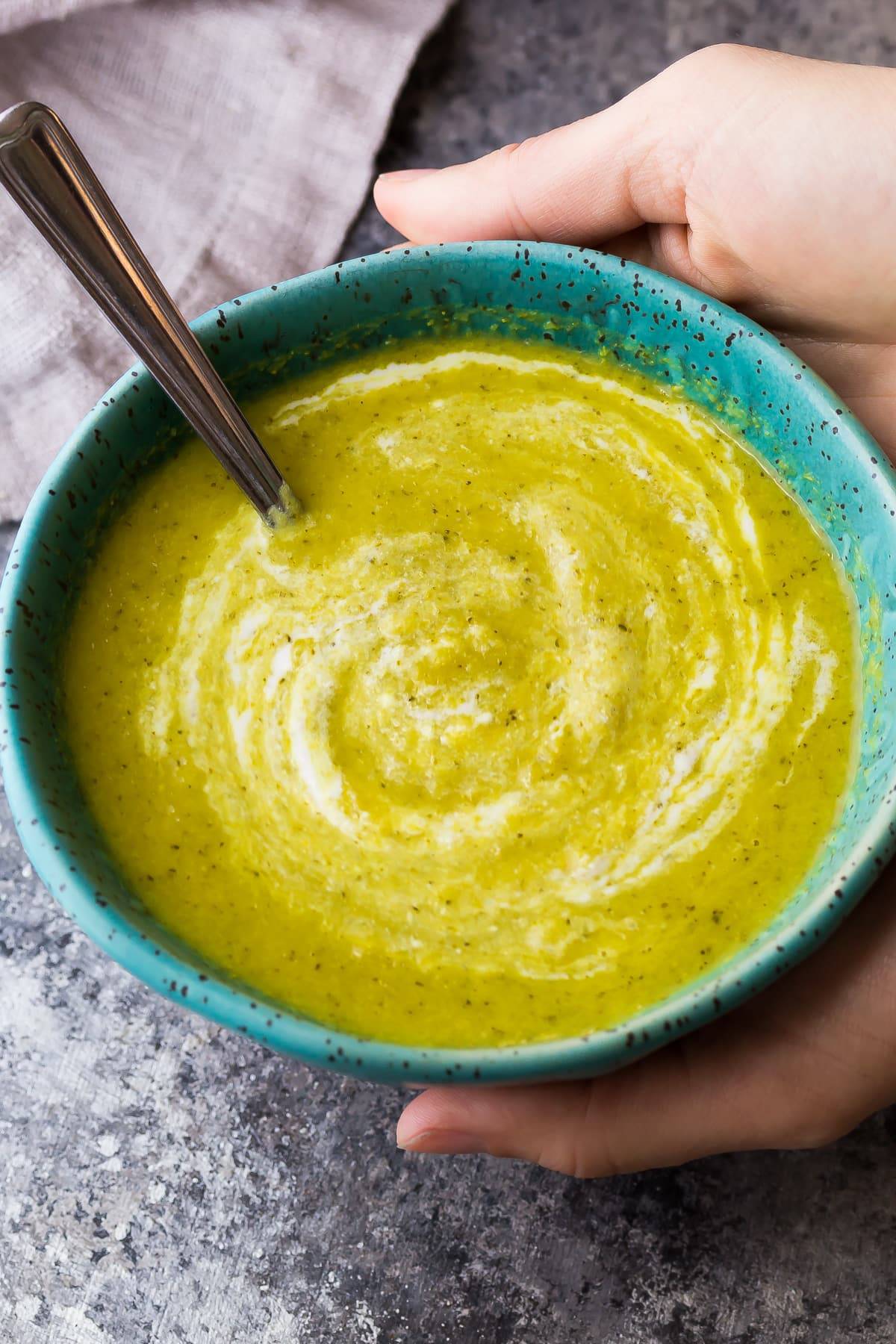 broccoli ginger soup in blue speckled bowl with a spoon stuck in the soup