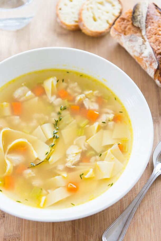 quick chicken noodle soup in white bowl with crusty bread in the background