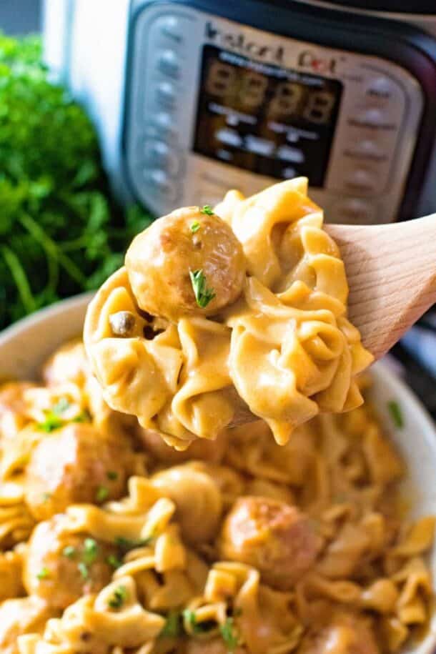 instant pot swedish meatballs close up on wooden spoon with pressure cooker in the background