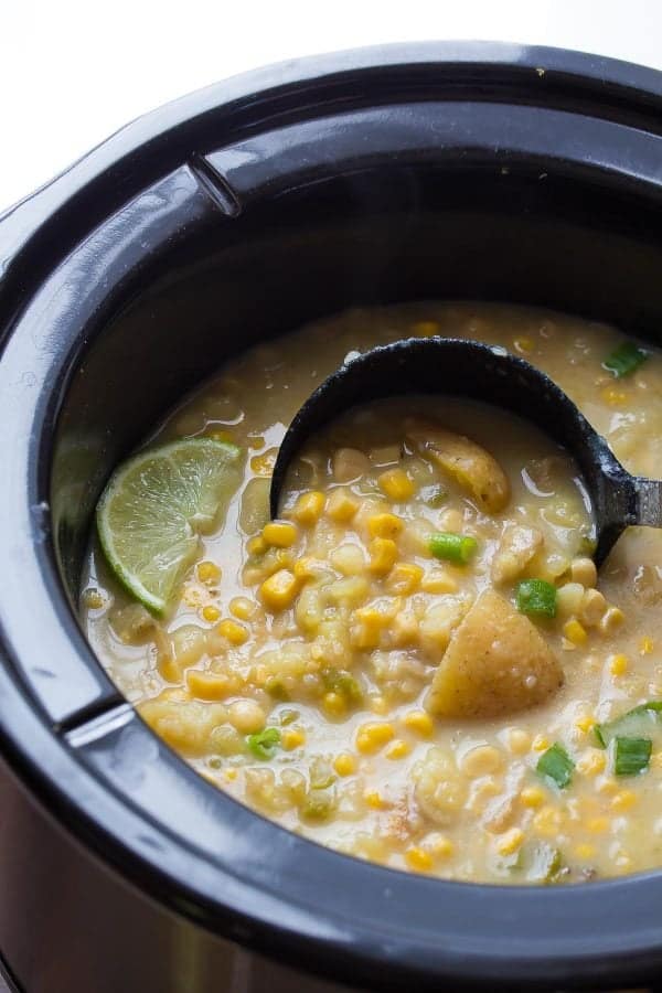 slow cooker potato corn soup in black slow cooker with a black scoop in the soup