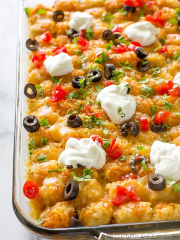 taco tater casserole in clear glas sbaking dish with olives and dollops of sour cream on top