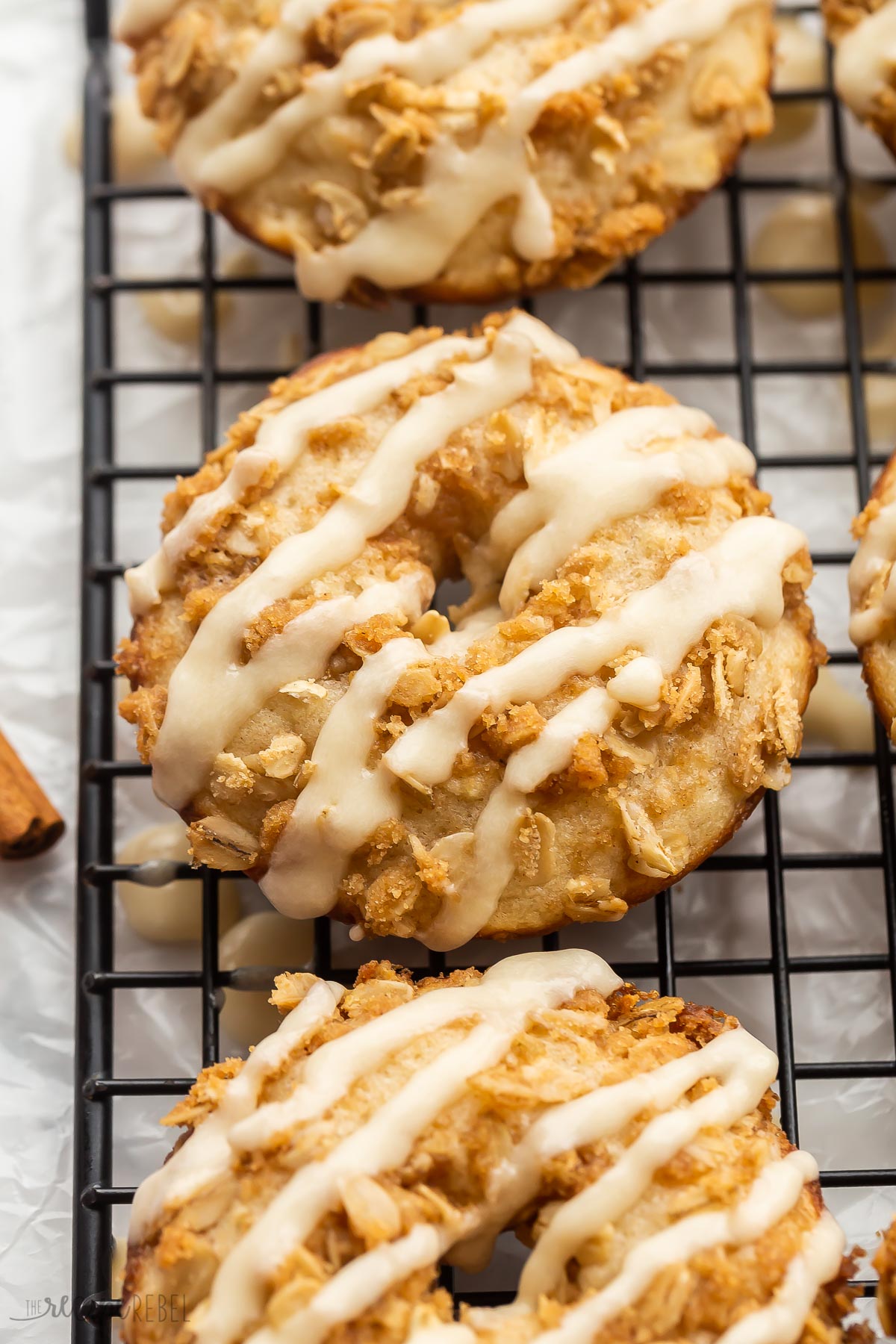 close up image of apple crisp donut with glaze on black cooling rack.